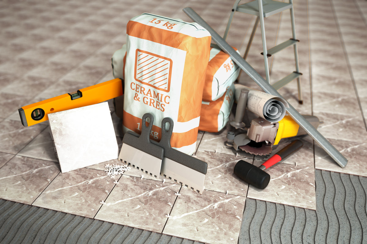 Professional tile installation workspace with notched trowels, tile spacers, spirit level, adhesive bags, and cutting tools on partially tiled floor.