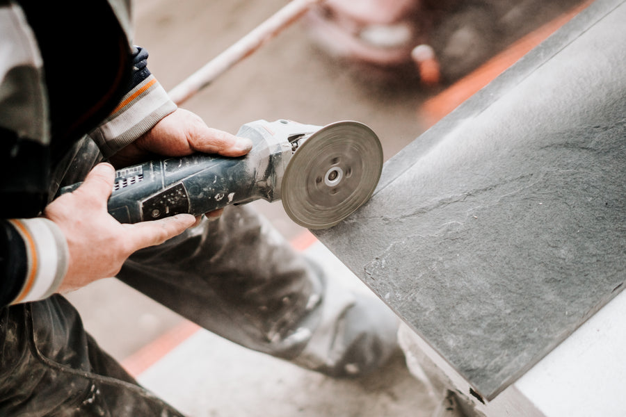Tile installer using an angle grinder power tool with spinning disc to cut a dark grey tile during installation