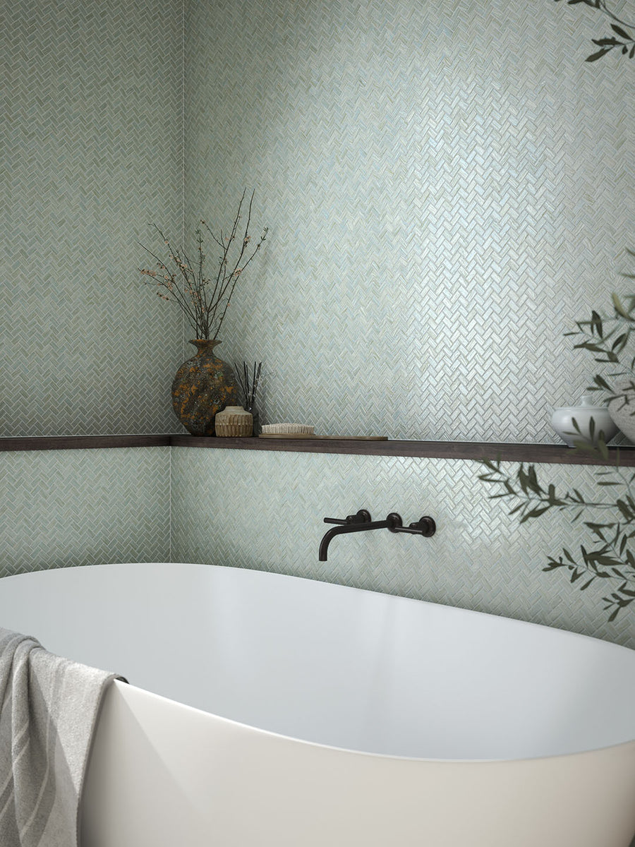 ElitTile Tile & Stone collection: serene bathroom with white tub, light green herringbone wall tiles, wood shelf.