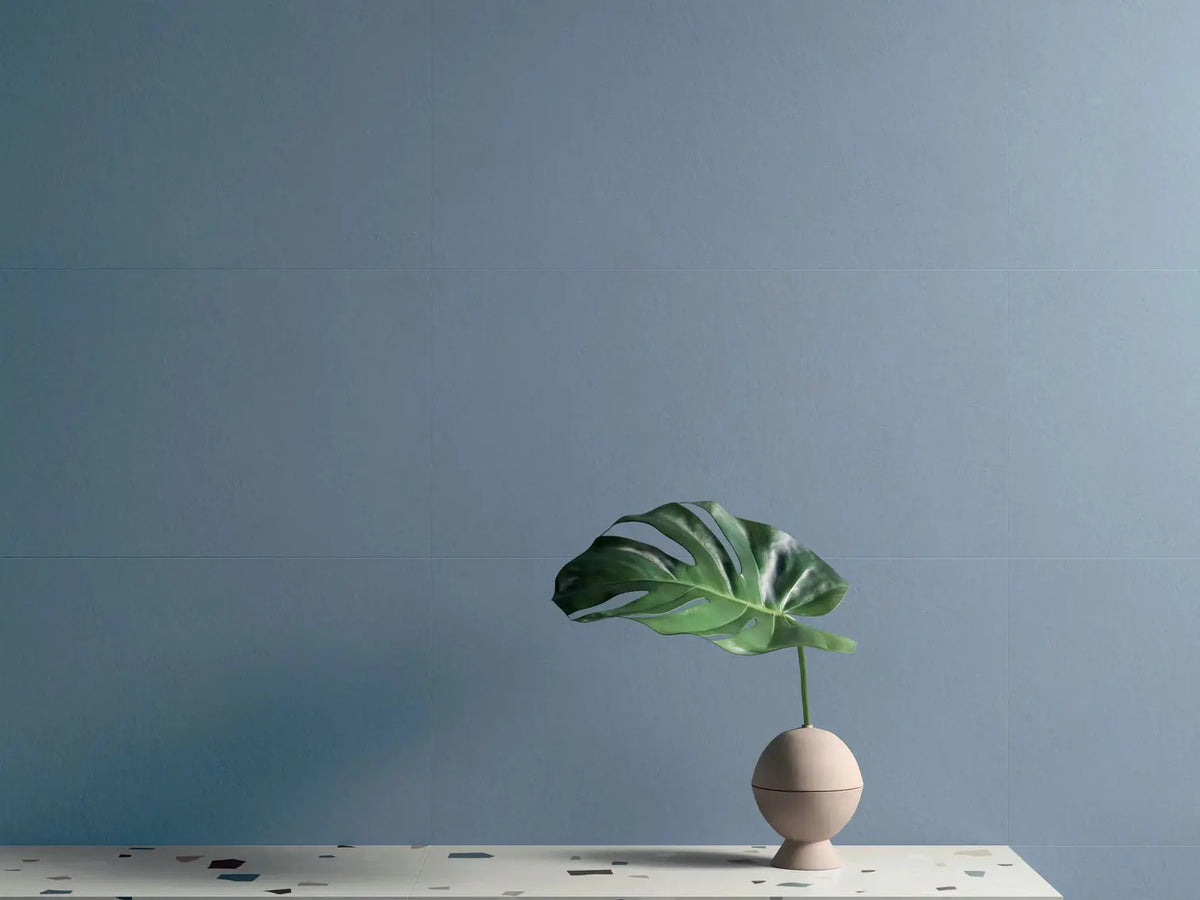 Minimalist interior with Nuances Cielo & Grigio tiles, terrazzo countertop, beige spherical vase, and dark green Monstera leaf