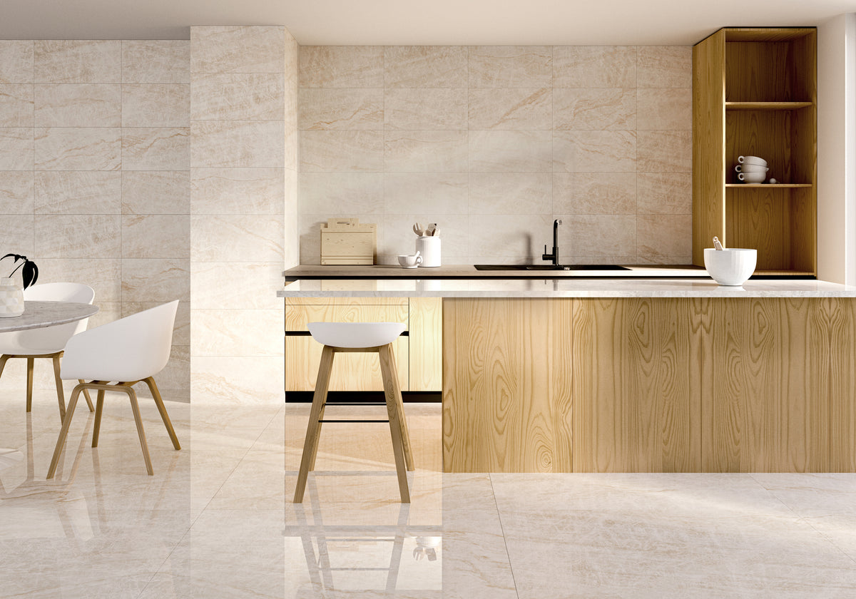 Modern kitchen with light wood cabinetry, cream travertine-style tiles on walls and floor, dark countertops, kitchen island with breakfast bar, and round dining table with white chairs