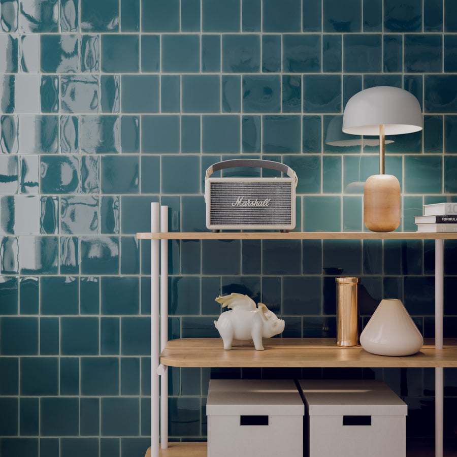 ElitTile Tile & Stone glossy teal-green subway tiles on wall, wooden shelves with speaker, lamp, books, and decor.