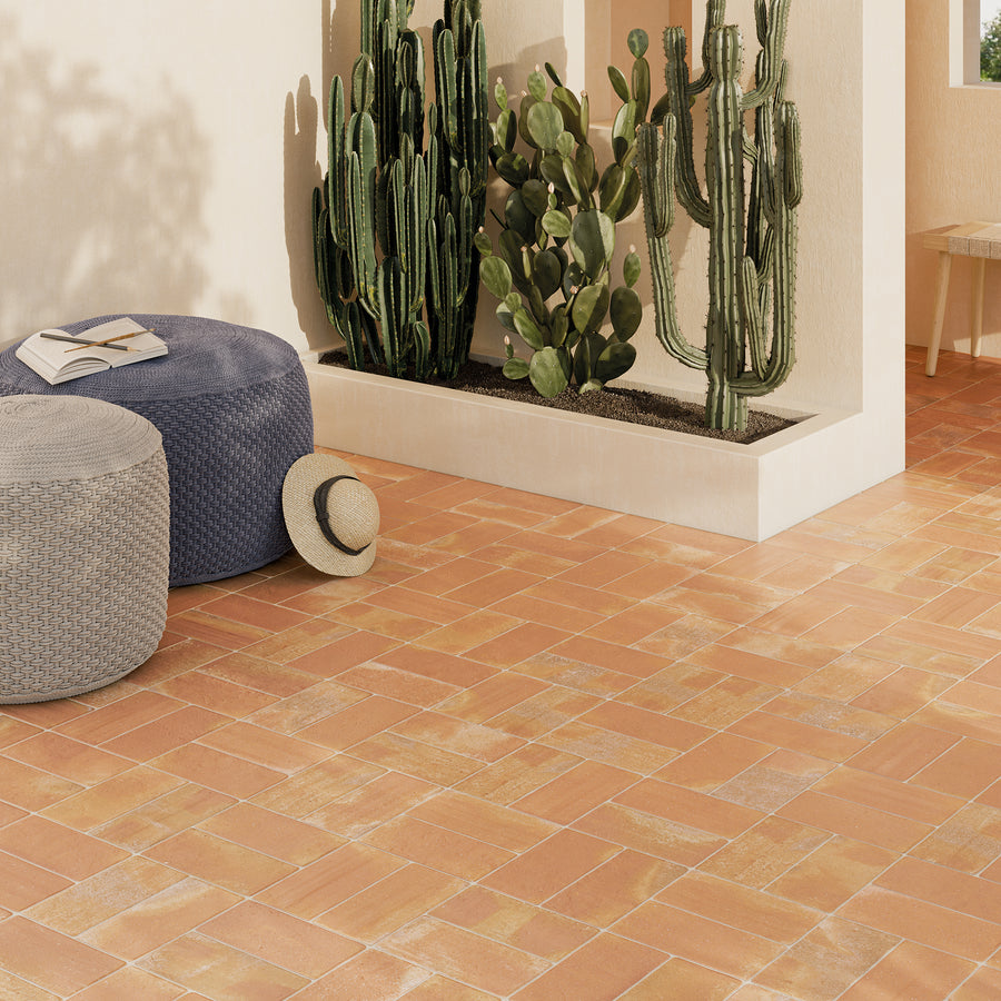 ElitTile Tile & Stone terracotta herringbone floor tiles on a sunny patio with large cacti and woven poufs.