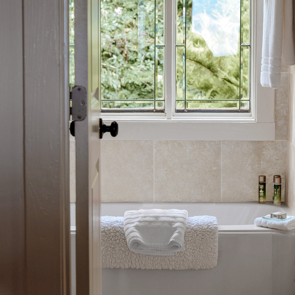 Bathroom showcasing ElitTile Tile & Stone light travertine natural stone wall tiles, a tub, and a window.