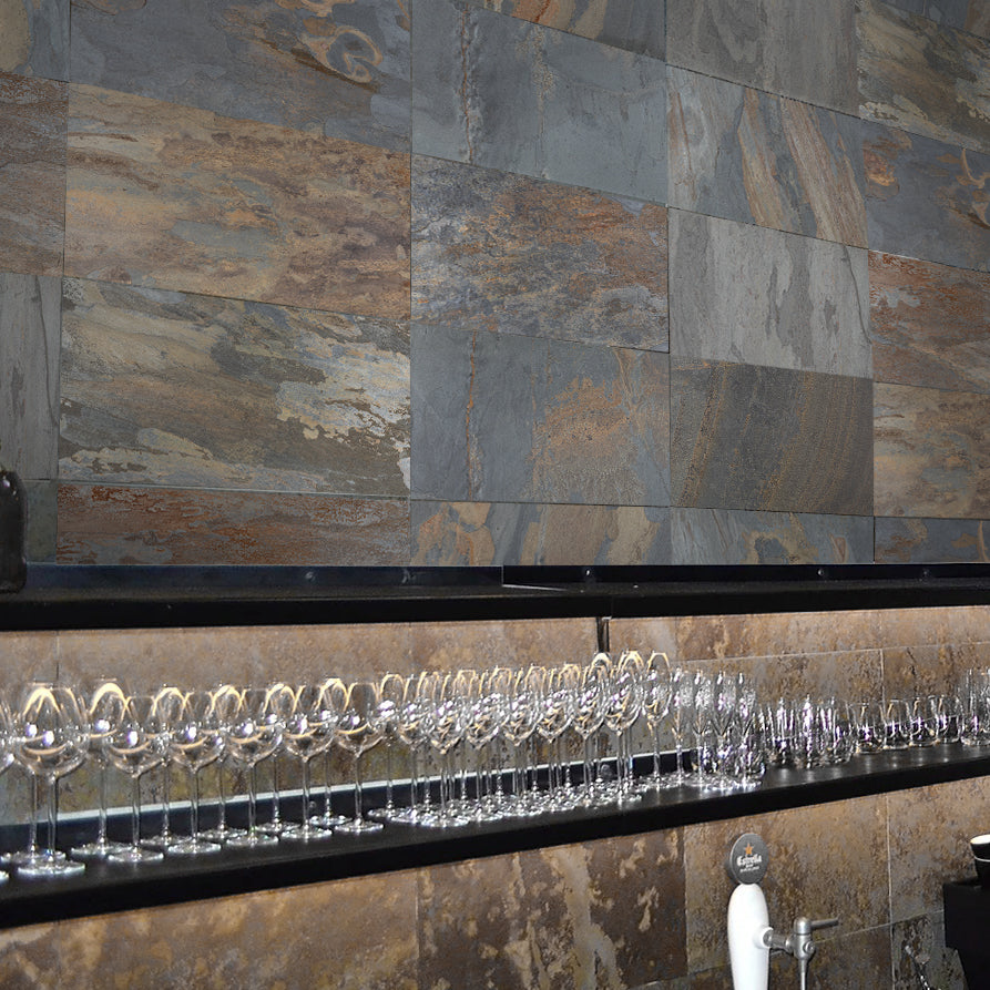 Bar area featuring ElitTile Tile & Stone multi-colored slate natural stone wall tiles, dark counter, and clear glasses.