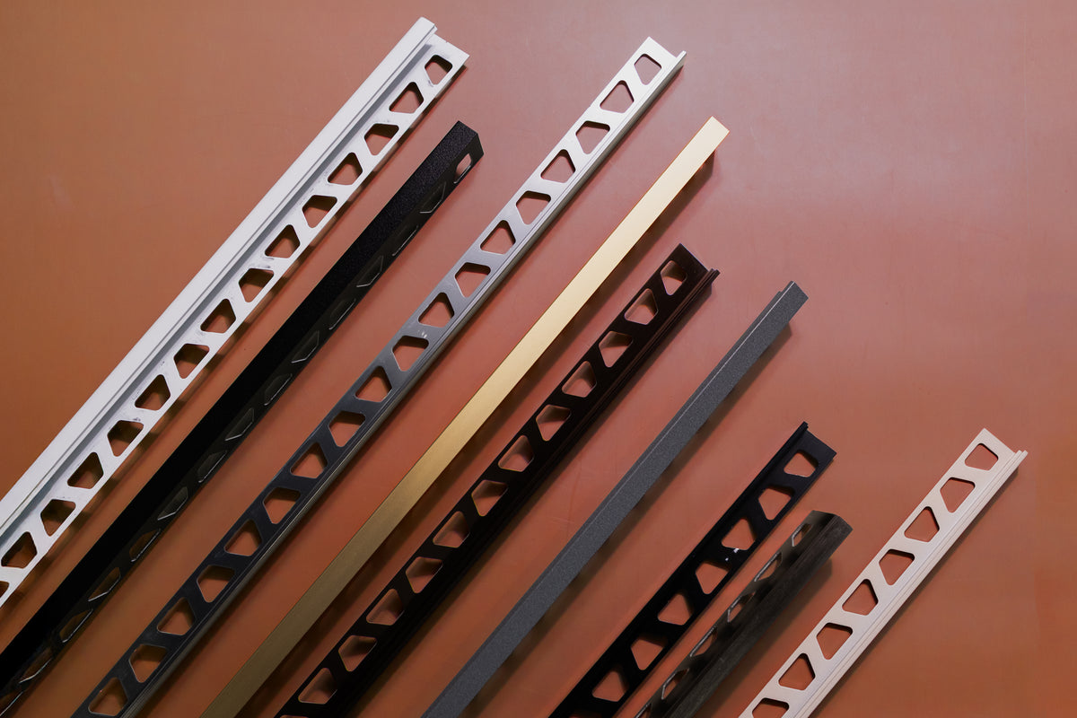 Collection of metal tile edge trims and profiles in various finishes including white, black, silver, gold, and beige with L-shaped designs