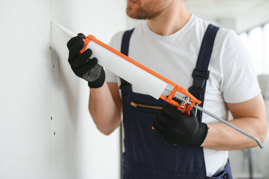 Professional applying white caulk sealant to wall using orange caulk gun