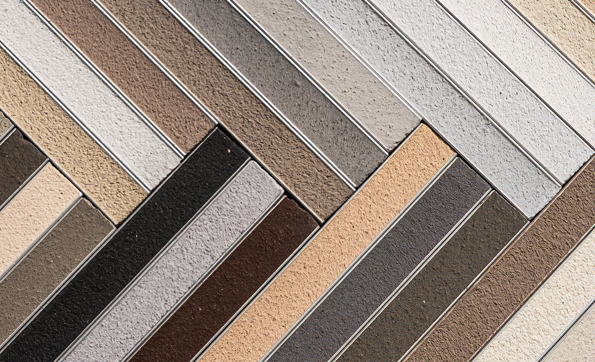 Tile sample board displaying Grout collection in herringbone pattern, featuring neutral tones of beige, brown, grey, and black with metallic separators